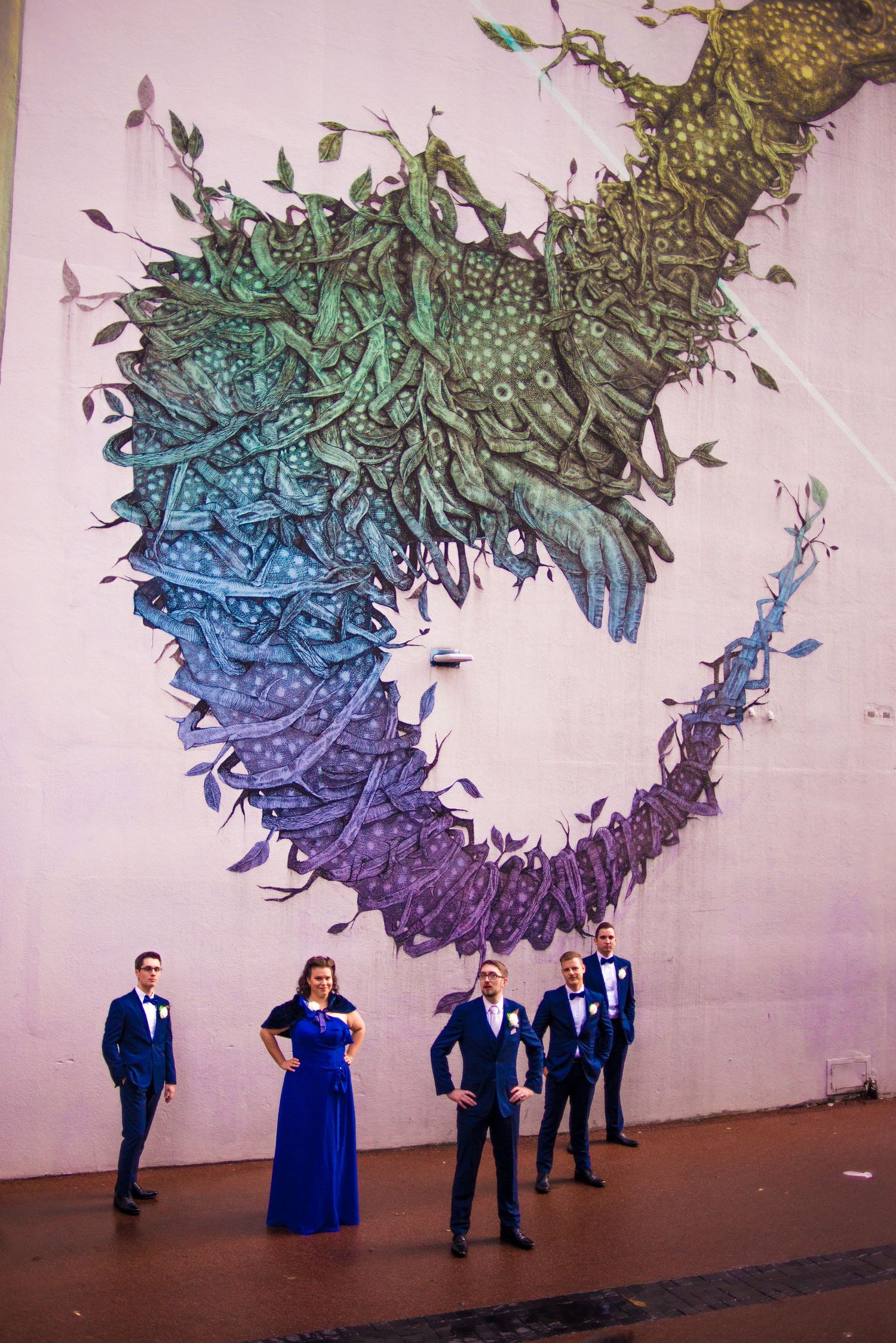 Wedding party poses beneath a large gradient wall mural featuring cascading organic shapes.