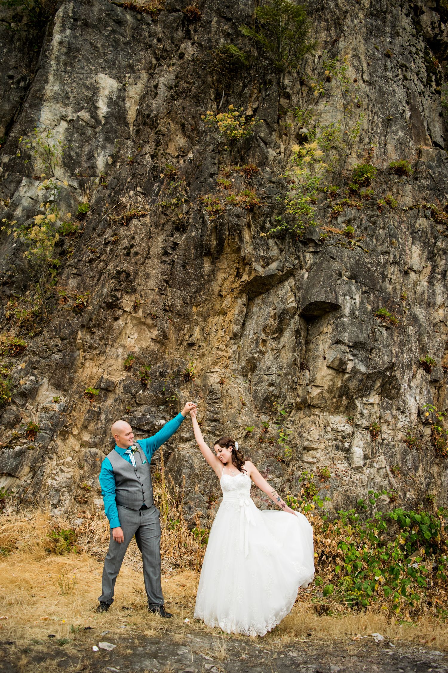Dancing pose against dramatic cliff face during outdoor wedding photography.