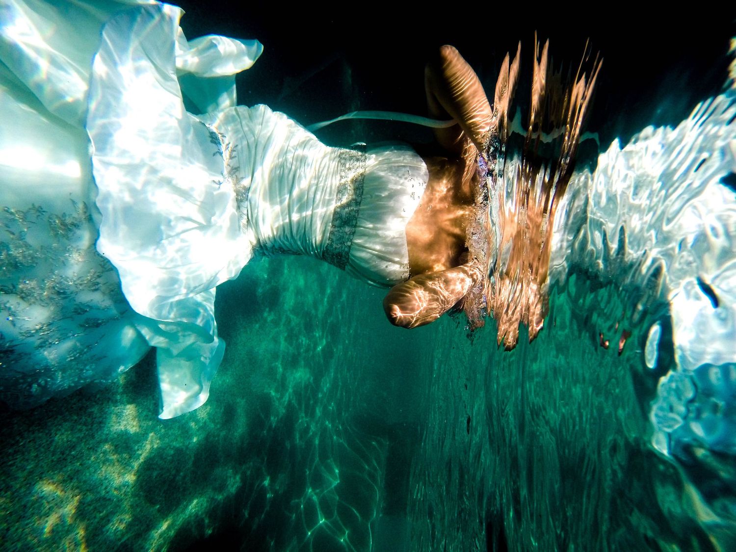 An underwater photo showing a person swimming beneath glowing blue-green ice formations.