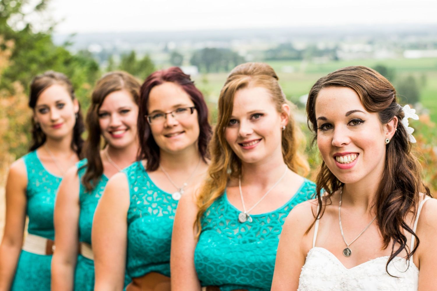 Bridesmaids in matching turquoise lace dresses pose together outdoors.
