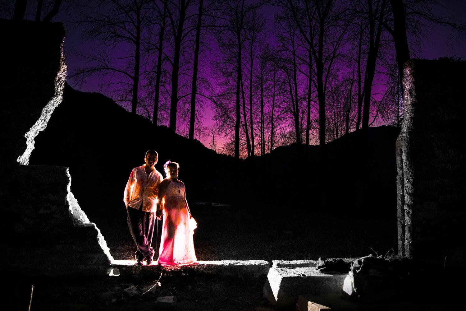 Dramatic night portrait with couple illuminated against purple sky and dark trees.