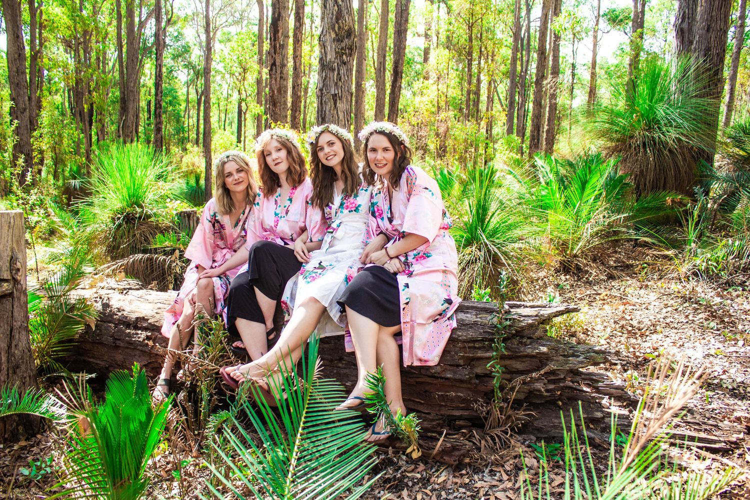 A group in matching pink robes sits together on a log in a lush forest setting.