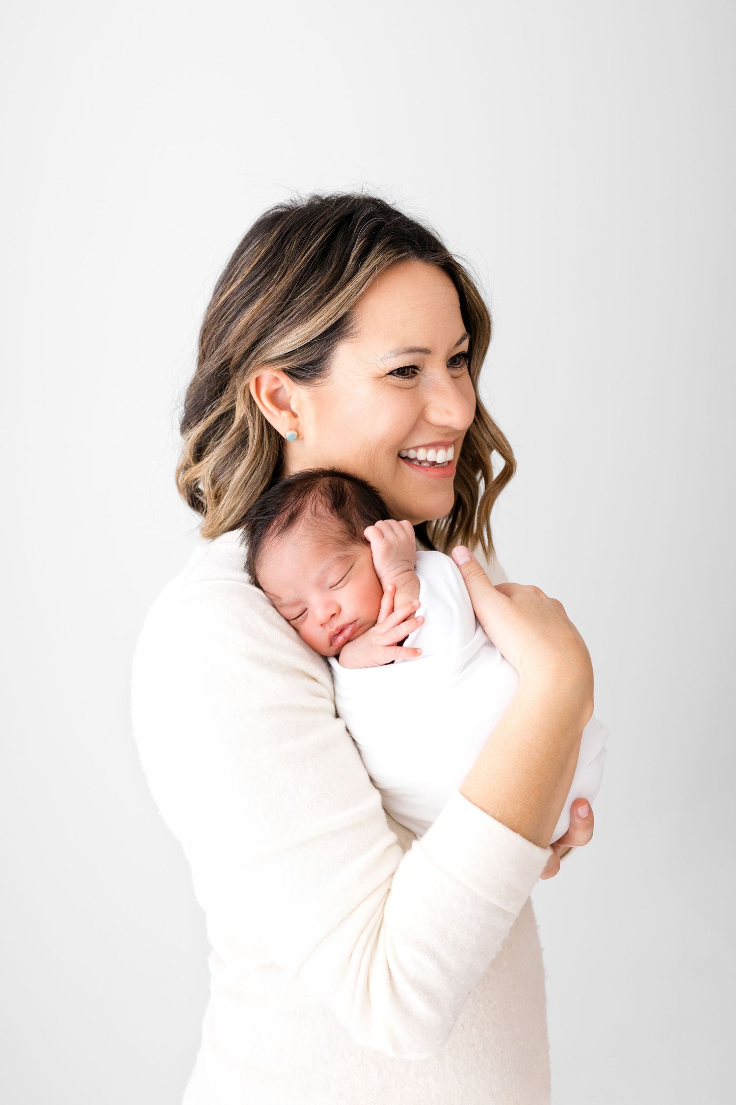 Mom smiling while holding her swaddled baby during her newborn photo session in Santa Fe, NM from Albuquerque.