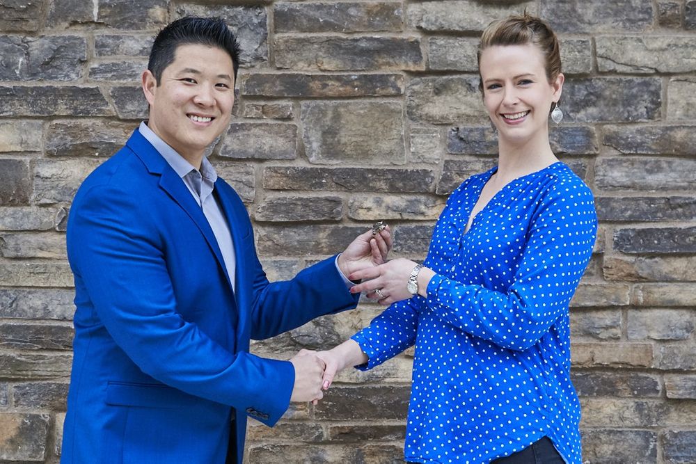 Portrait of male real estate agent in gorgeous blue suit handing keys to female client outside building Point Ruston