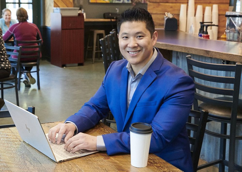 Portrait of male real estate agent in gorgeous blue suit inside coffee shop working at laptop