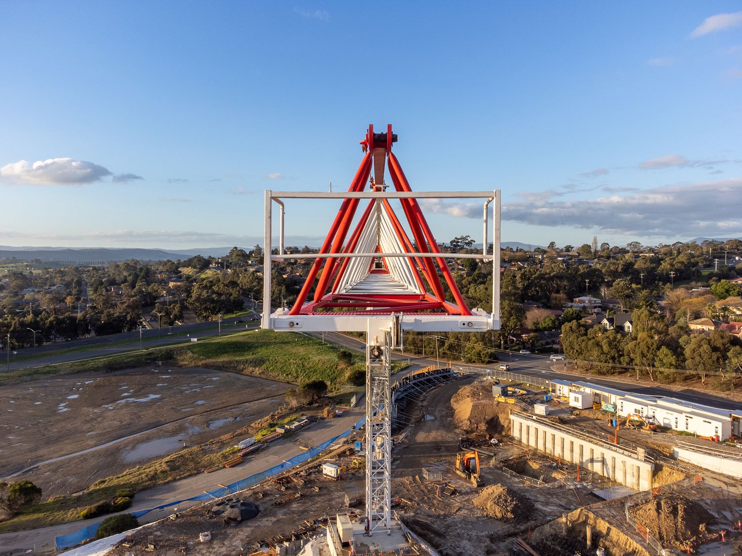 Aerial view of red triangular crane tower at suburban construction site at golden hour.
