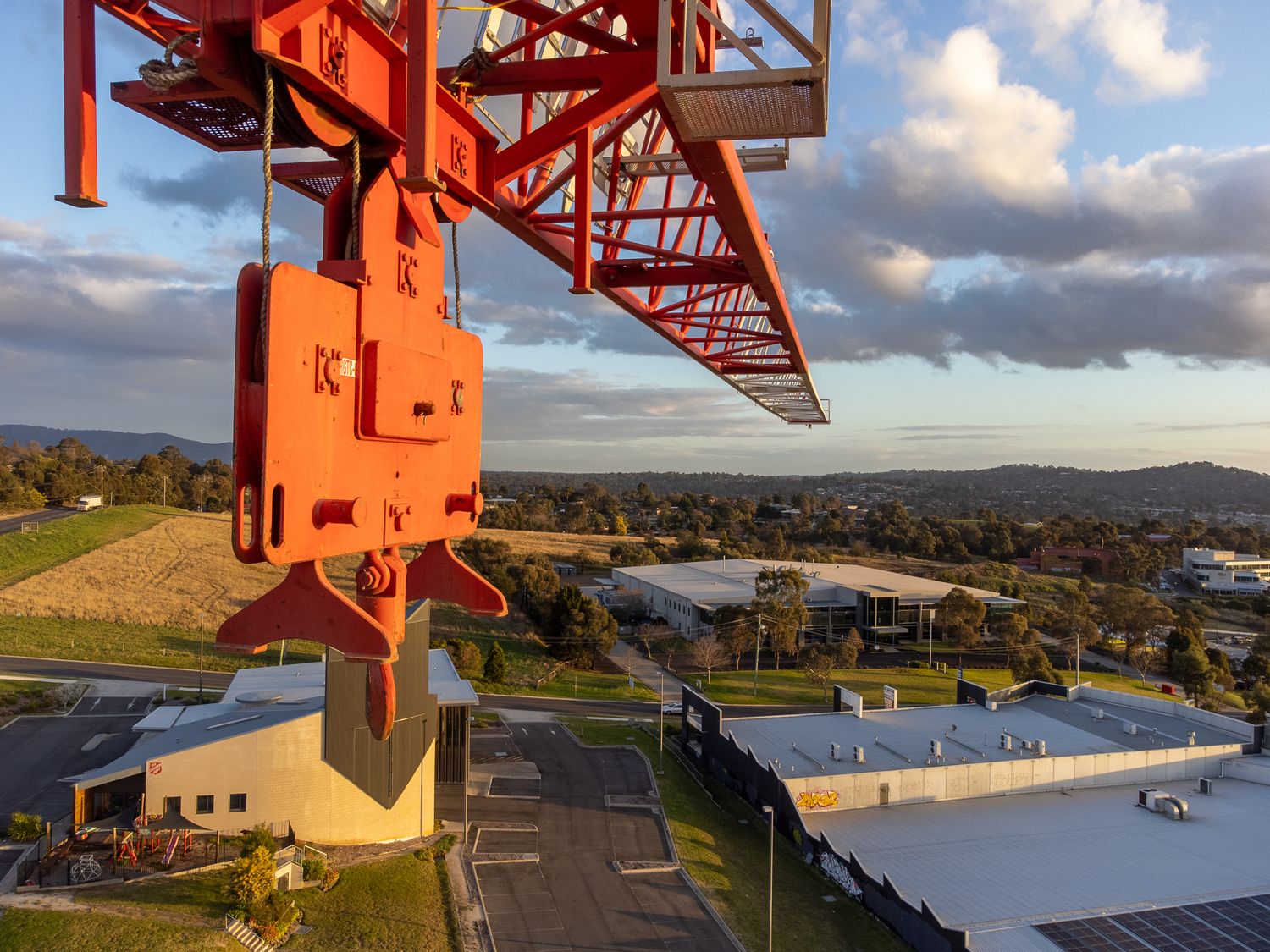Close-up of an orange tower crane hook and block against a suburban Australian landscape at golden hour.