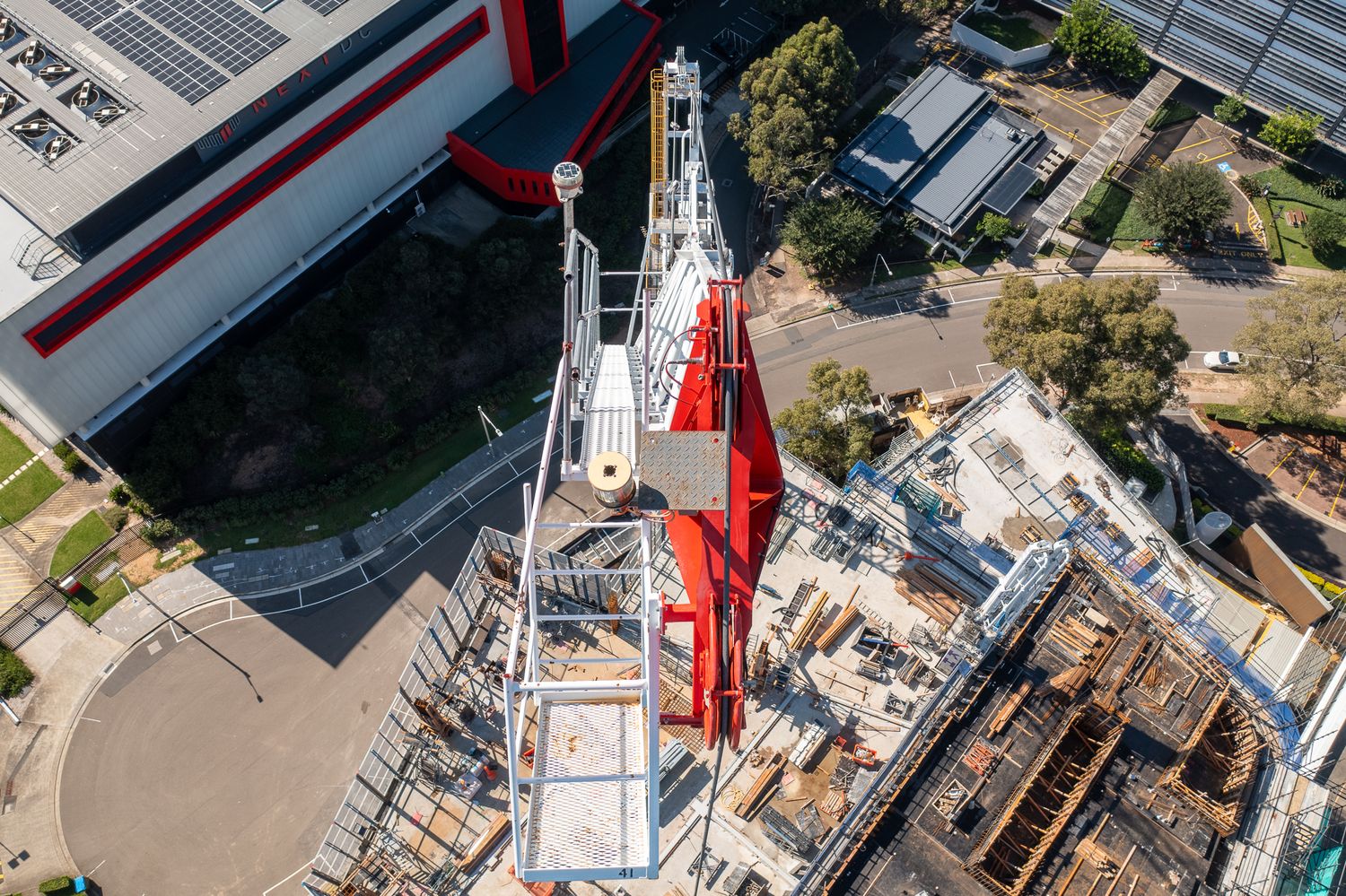 Aerial top-down view of a red and white tower crane over an active urban construction site.