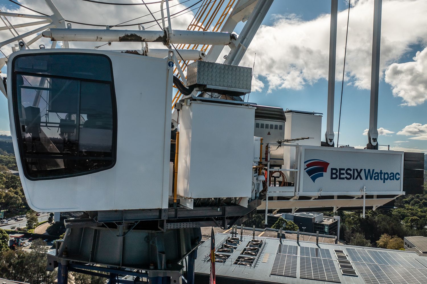 BESIX Watpac branded crane cabin with solar panels at a construction site under cloudy skies.
