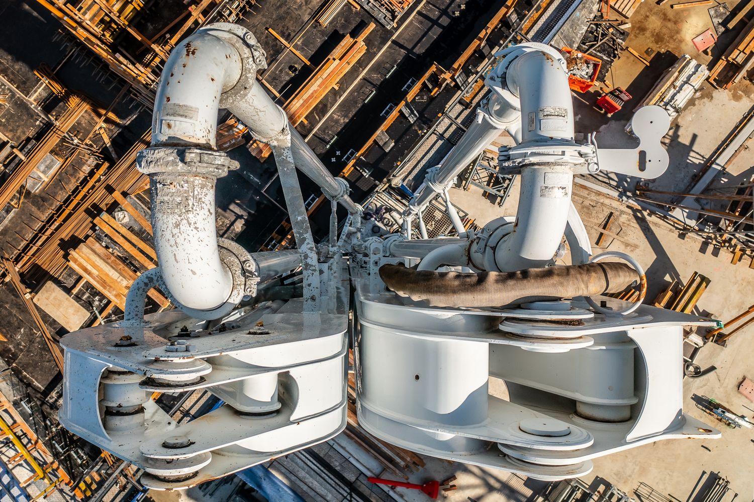 Aerial view of large white crane hook blocks and rigging over a busy construction site below.