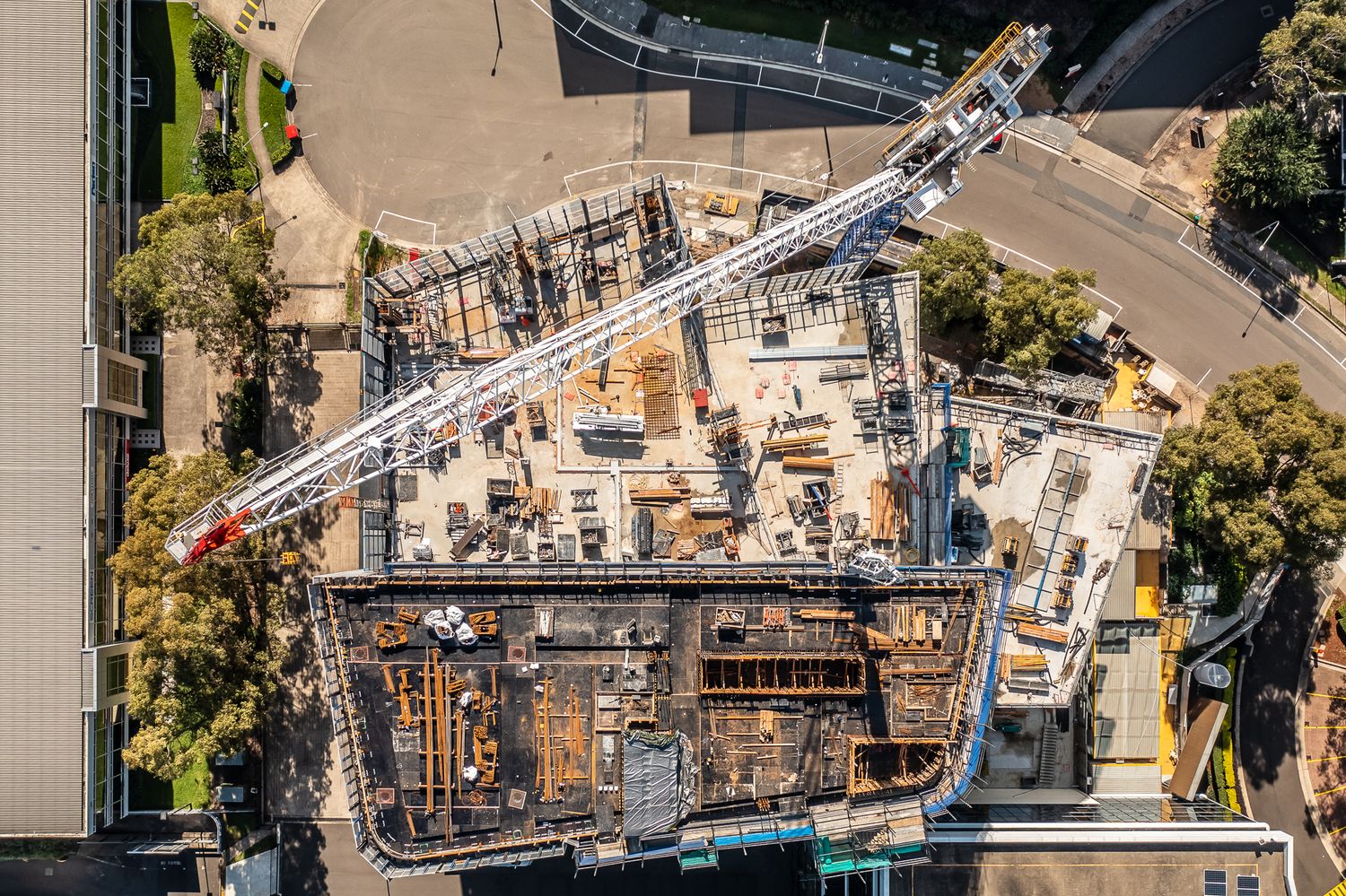 Aerial top-down view of an urban construction site with a large white crane and deep excavation.
