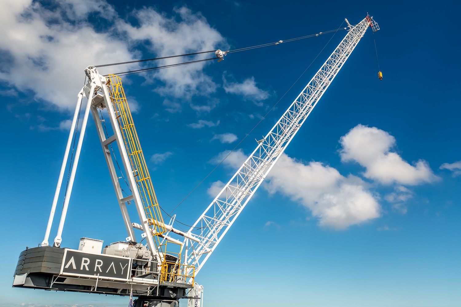 Array-branded luffing tower crane against a bright blue sky with white clouds.