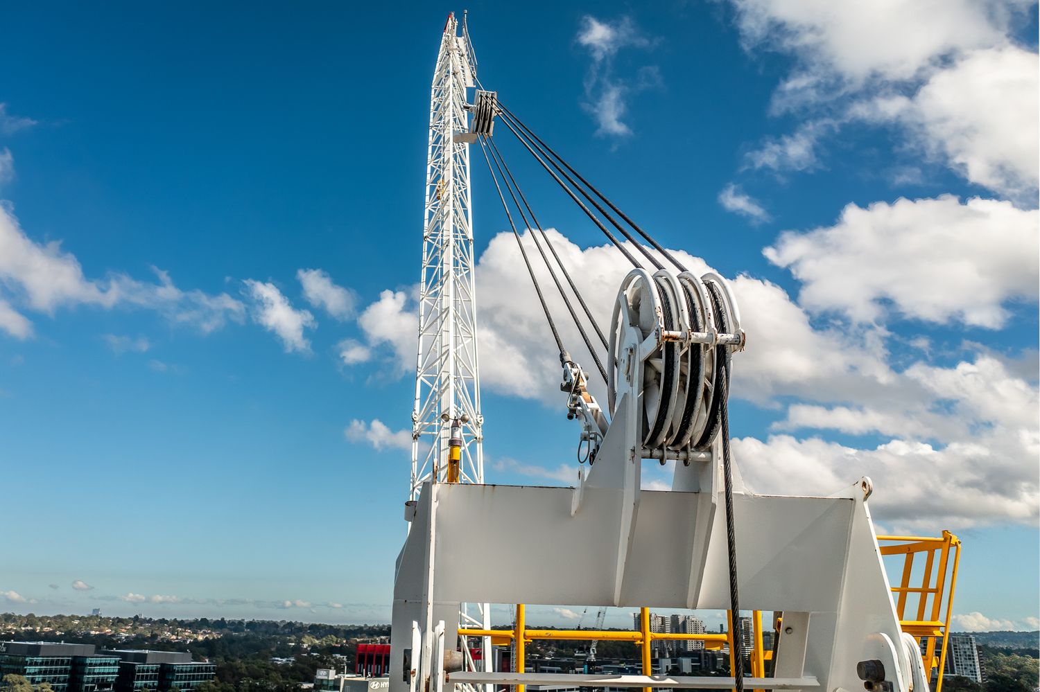 White crane mast and pulley block system against a blue sky at a construction site.