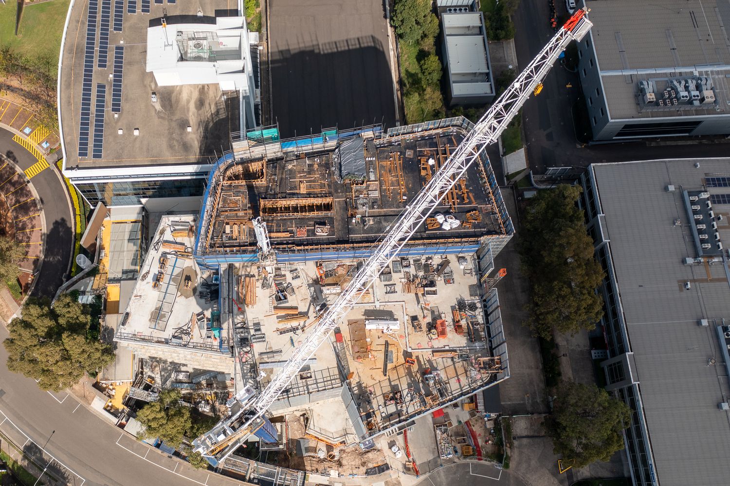 Aerial view of an active urban construction site with a white luffing crane and deep excavation.