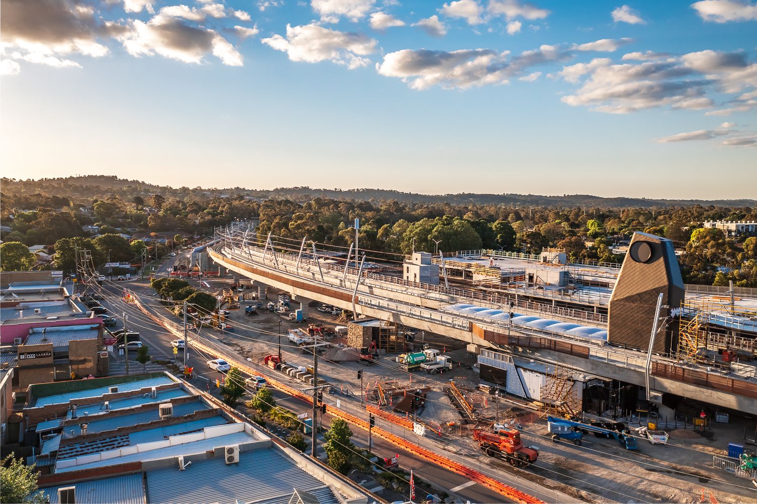 Aerial view of elevated railway construction site at sunset in suburban Australia with active road traffic below.