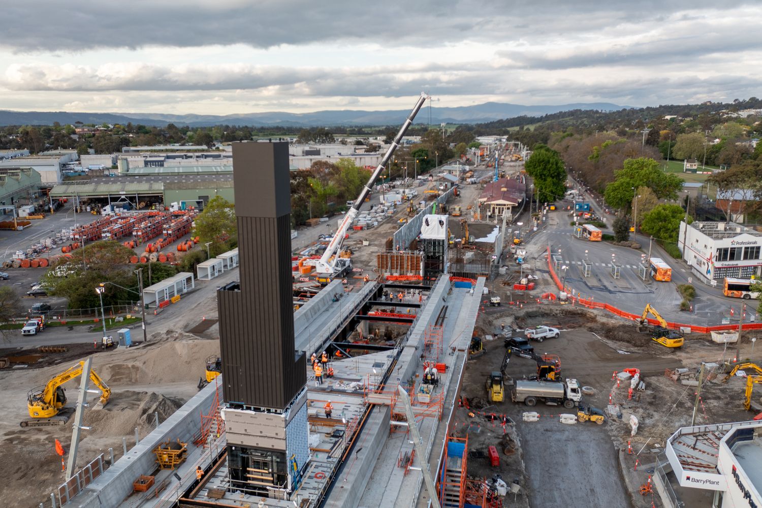 Aerial drone view of railway station construction with tall lift shaft and cranes in Australian suburb.
