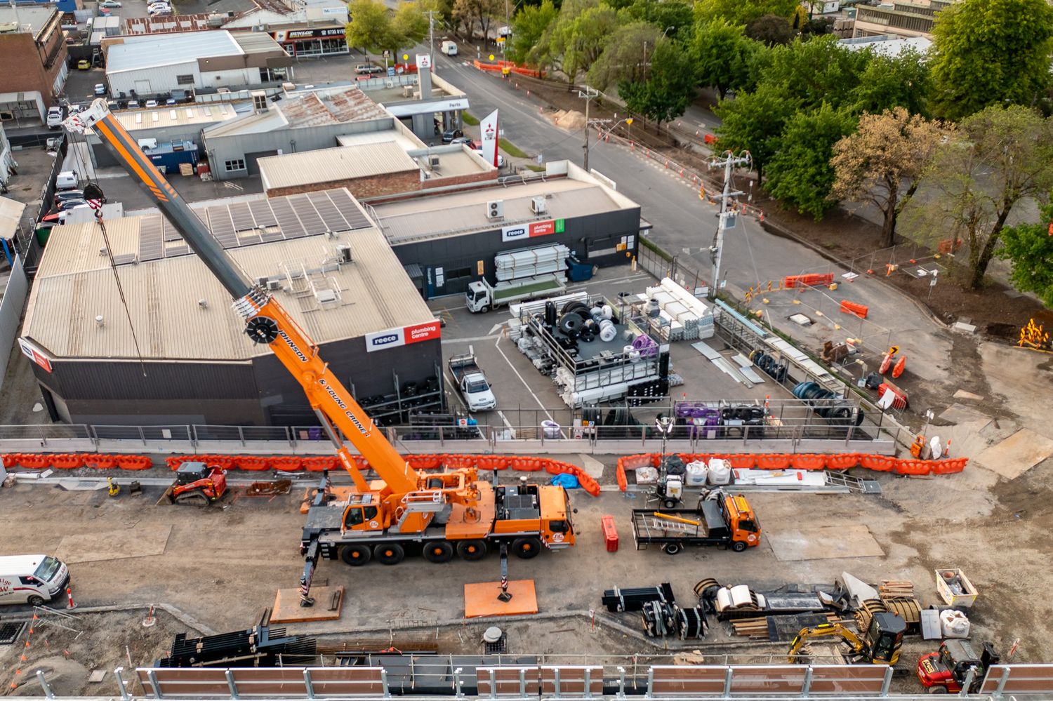 Large orange mobile crane at urban railway construction site with equipment and machinery on ground level.