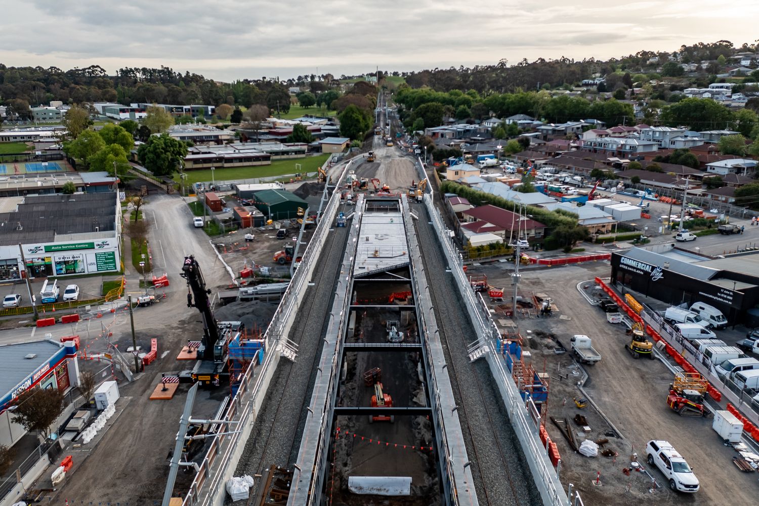 Aerial view of elevated railway track construction with concrete foundations and active building work in suburb.