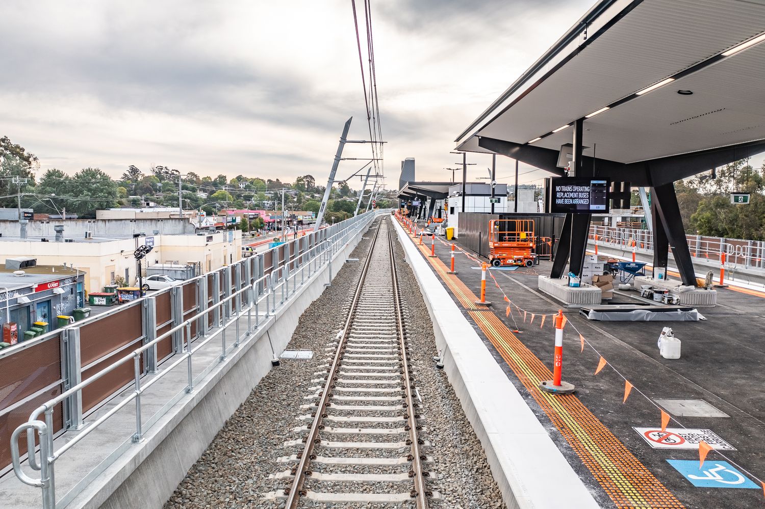 New elevated railway platform under construction with fresh track, safety barriers and station canopy installed.