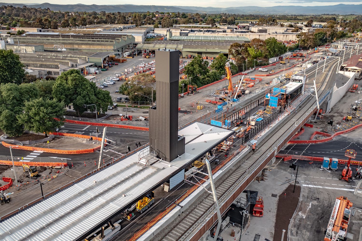 Aerial view of completed elevated railway station with platform canopies and tall lift tower at dusk.