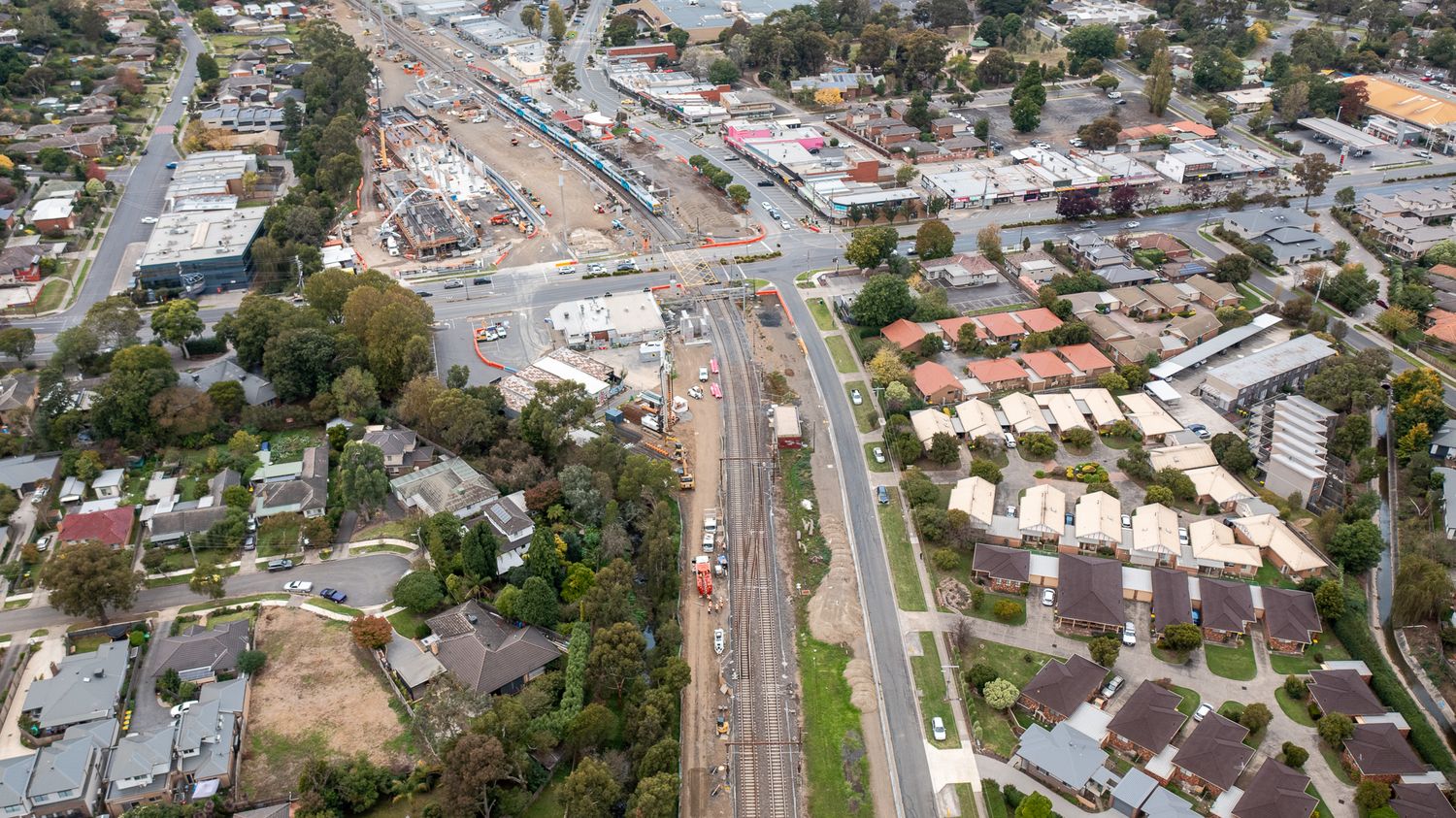 Aerial view of railway corridor construction through quiet Australian suburb with residential homes on both sides.
