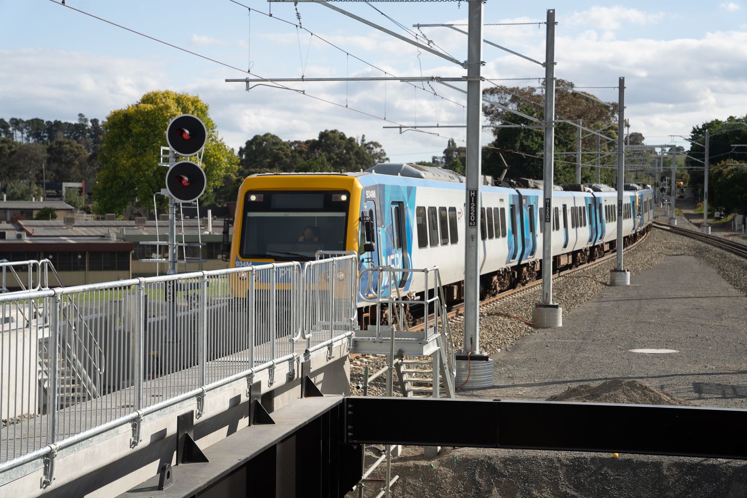 Yellow and blue metropolitan passenger train traveling along elevated rail tracks in suburban Australia.