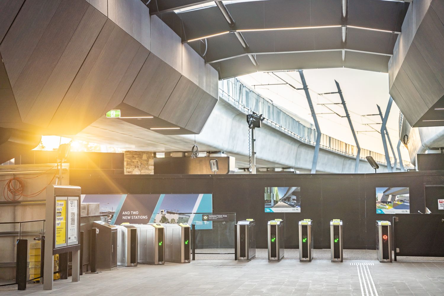 Modern train station interior with ticket barriers, geometric ceiling, and warm sunlight streaming through.