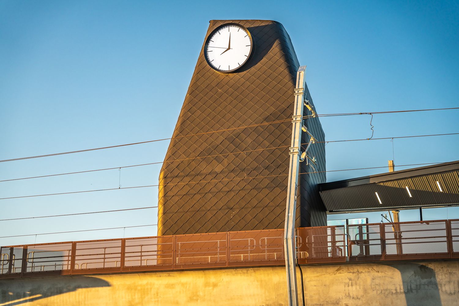 Distinctive train station clock tower with diamond-pattern facade against a clear blue sky.