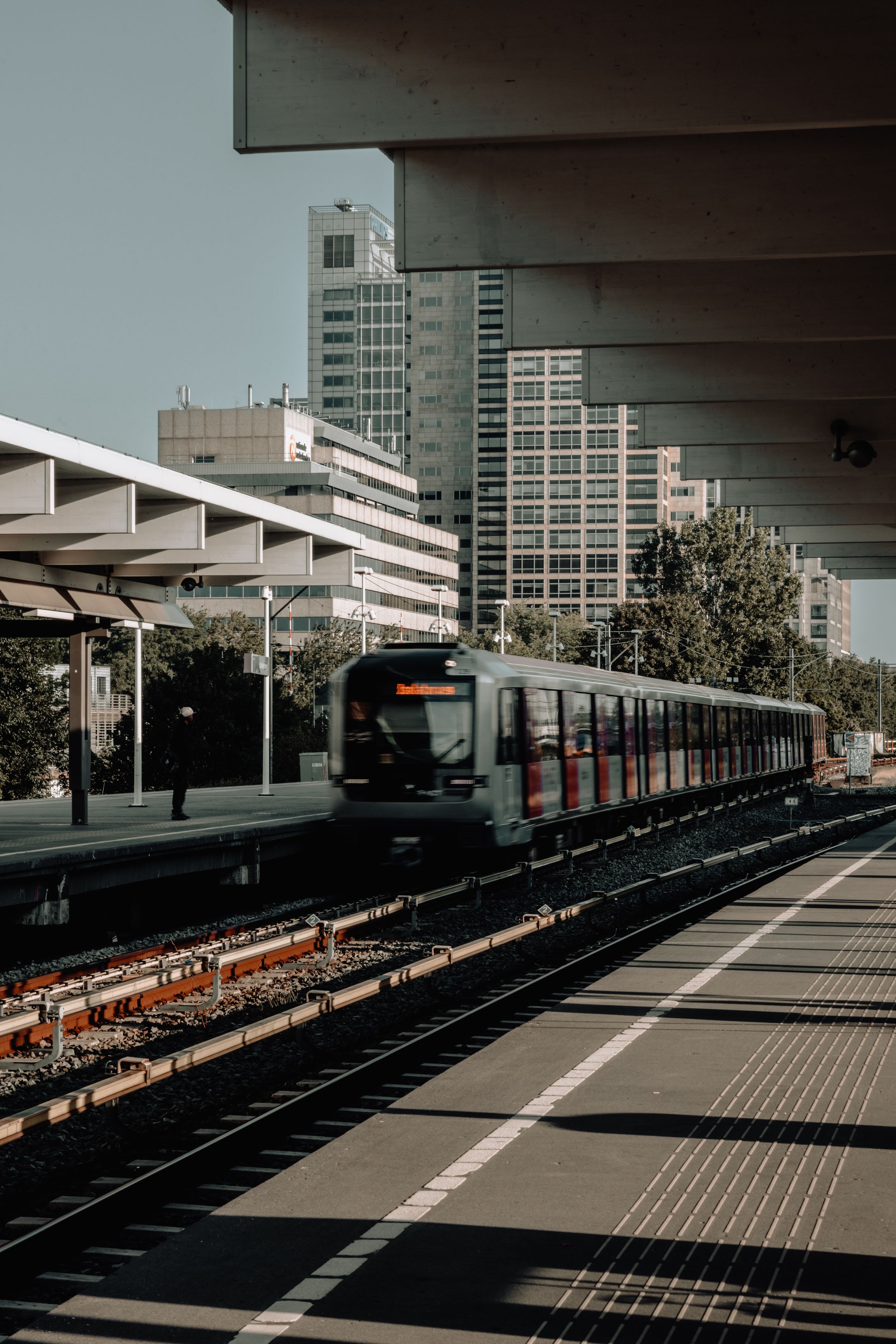 A modern train arrives at an urban transit station with high-rise buildings in the background.