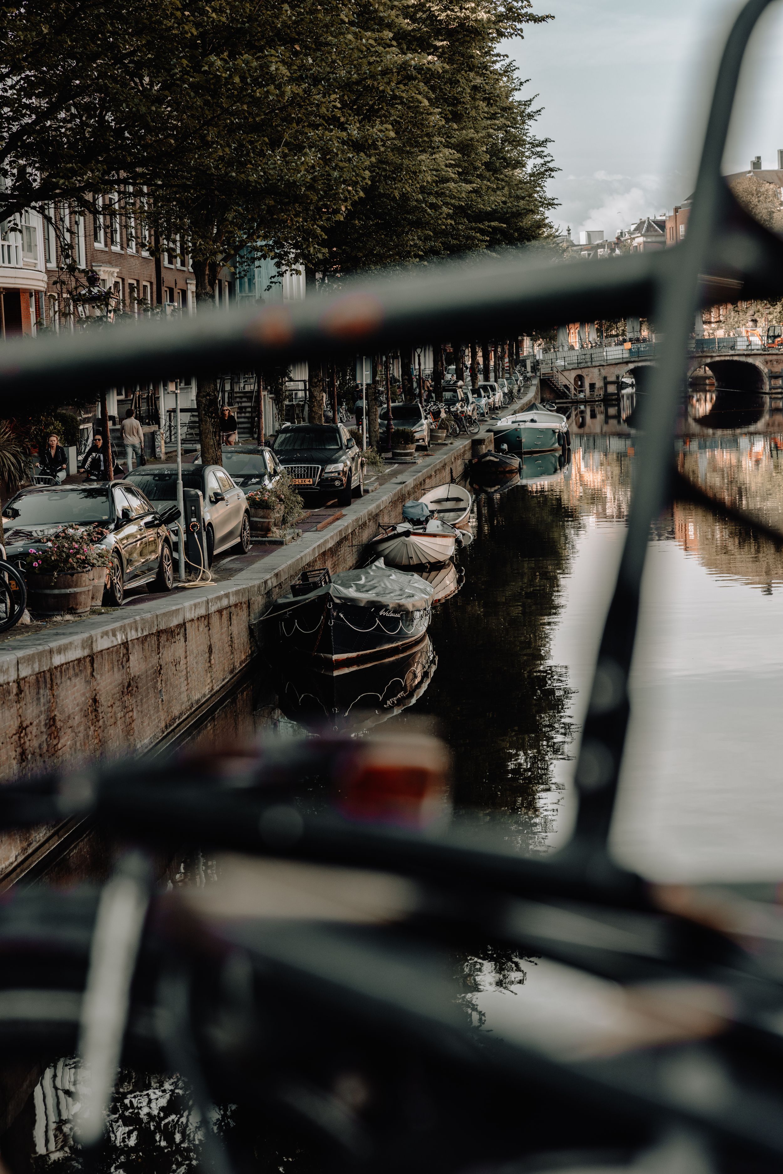 Canal view in Amsterdam with parked boats and cars along a tree-lined street.