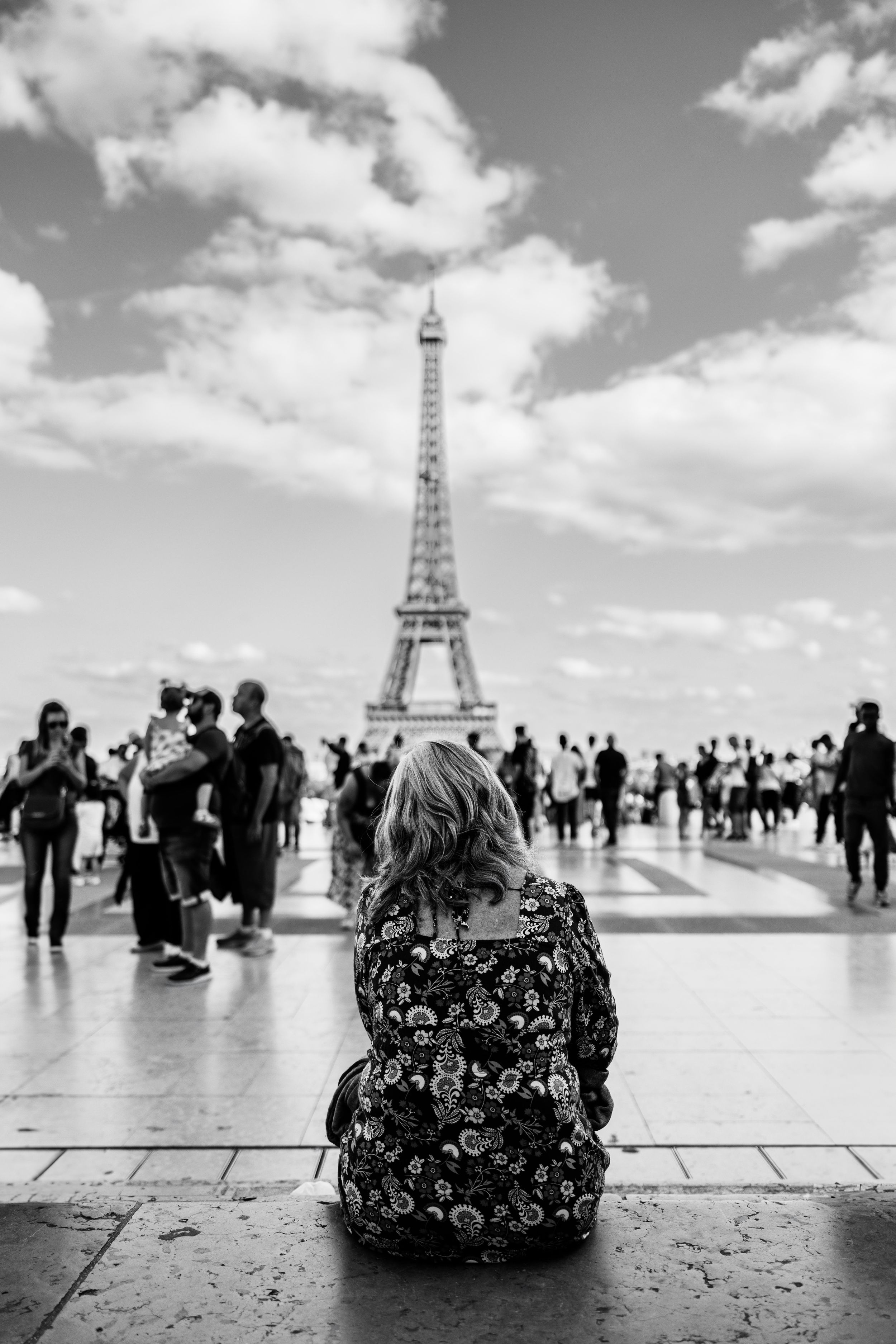 Black and white photo of a visitor admiring the Eiffel Tower from the Trocadero viewing platform.