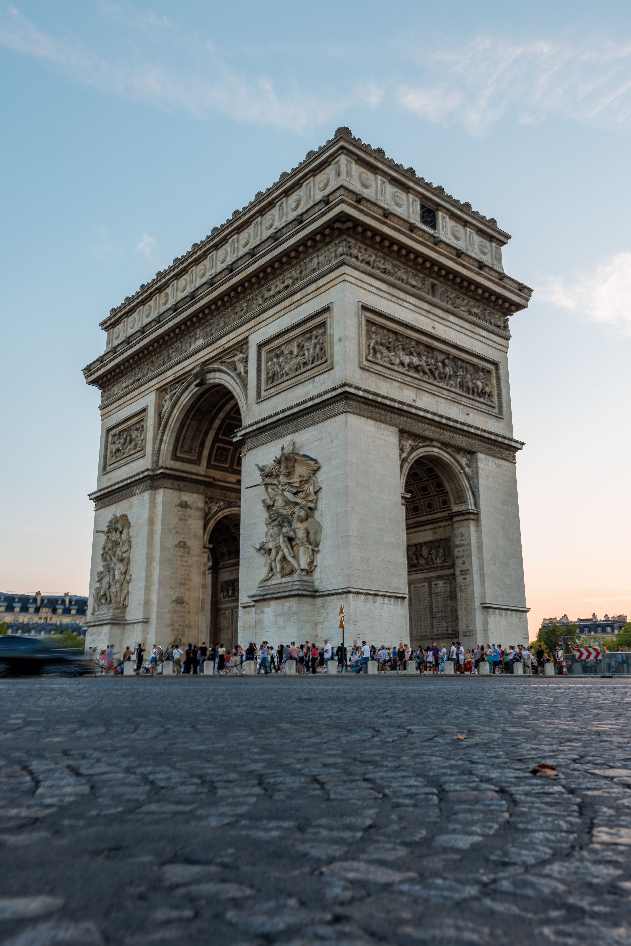 The Arc de Triomphe monument in Paris at sunset with tourists gathering below.