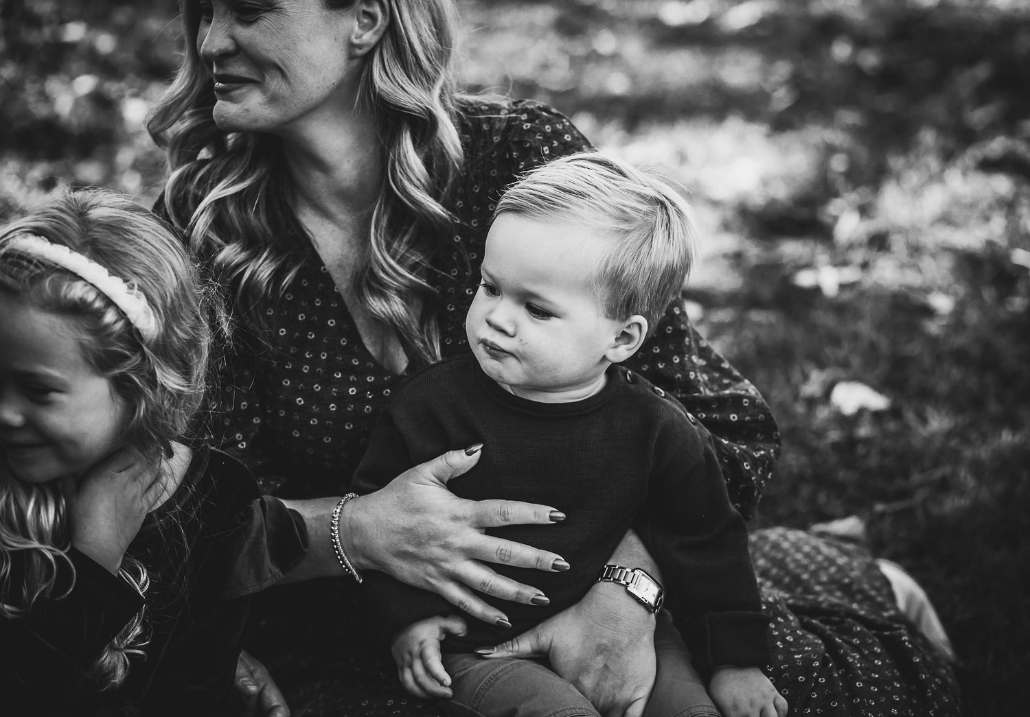 A tender black and white portrait of a parent holding children outdoors.
