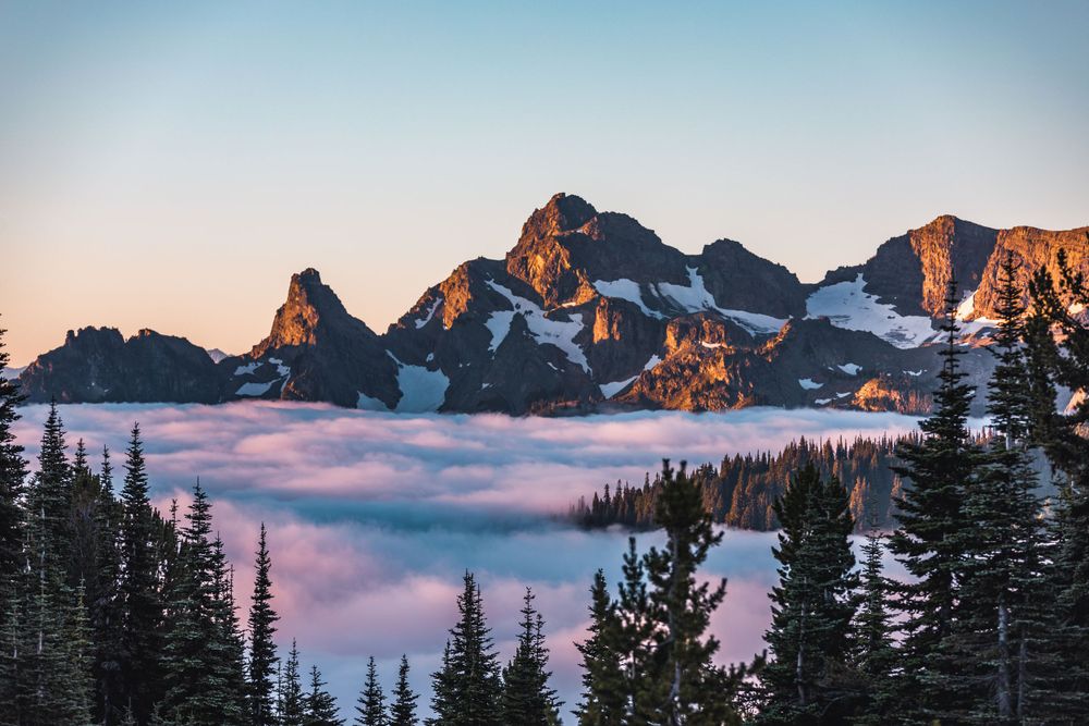 Mountain peaks rising above sea of clouds during colorful sunrise in alpine landscape.