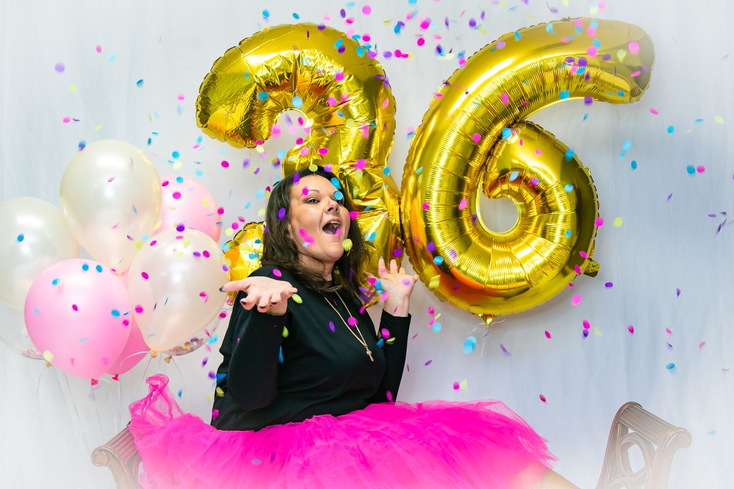 Birthday celebration with gold number 36 balloons and pink tutu against confetti background.
