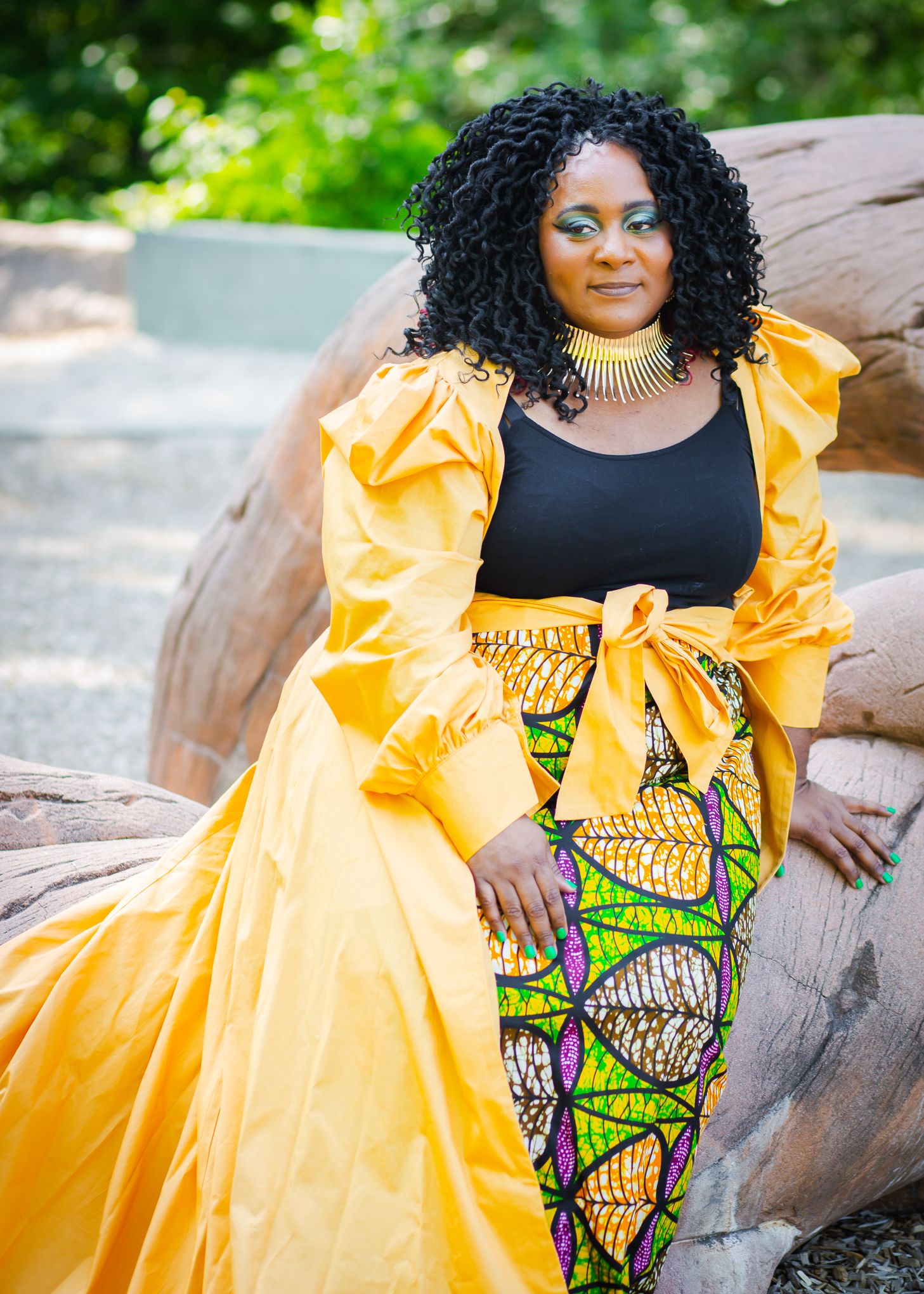 Fashion portrait in vibrant yellow dress with African print skirt against outdoor rocky backdrop.