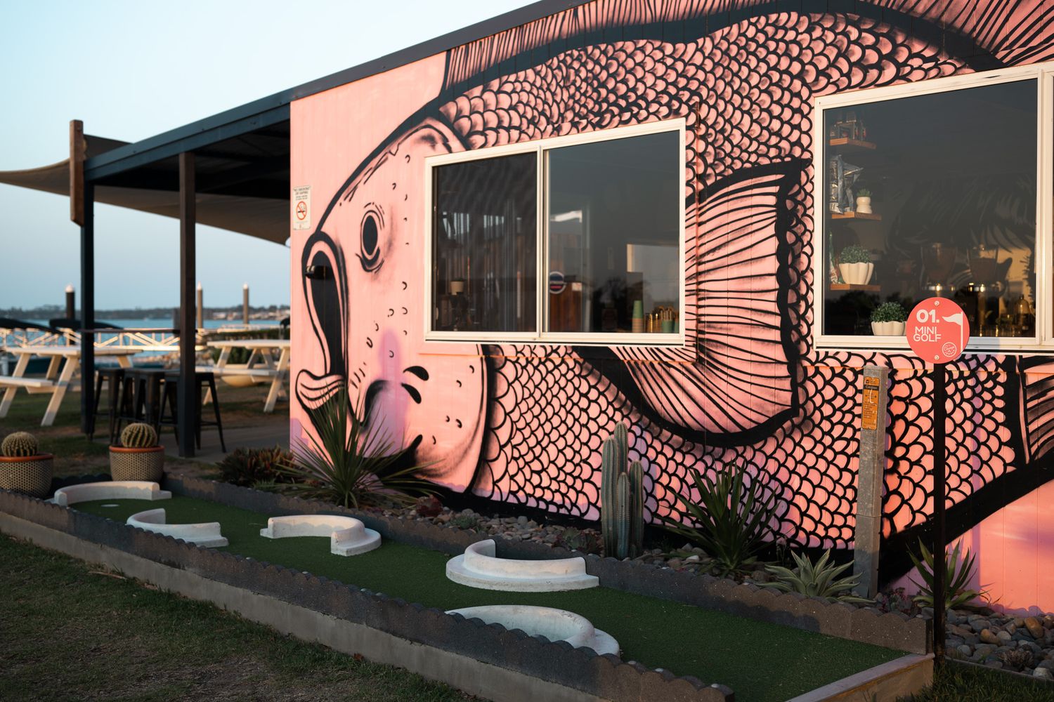Pink beach shack with artistic black pattern murals and outdoor seating area.