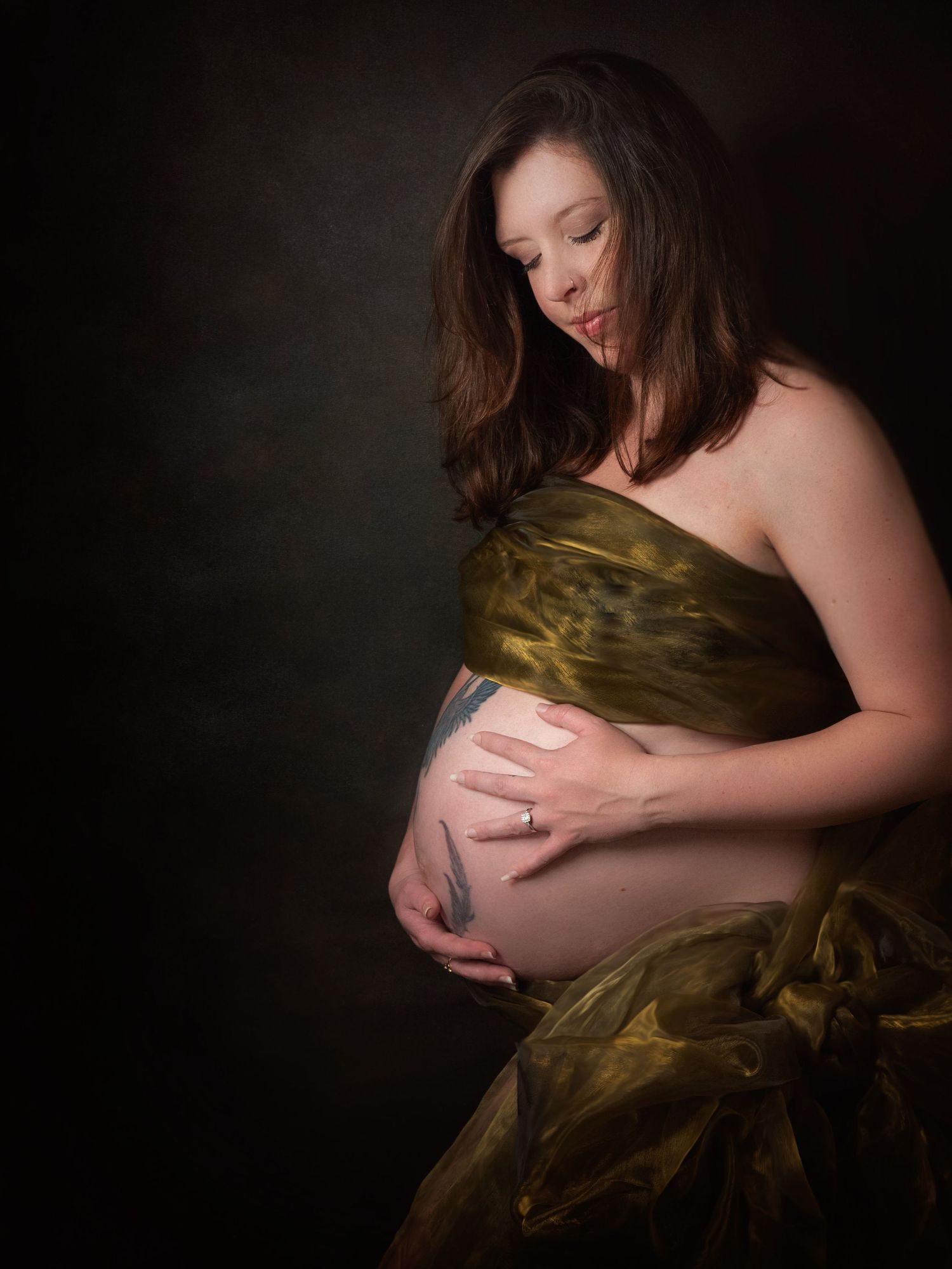 Pregnant lady holding her stomach looking down wearing gold