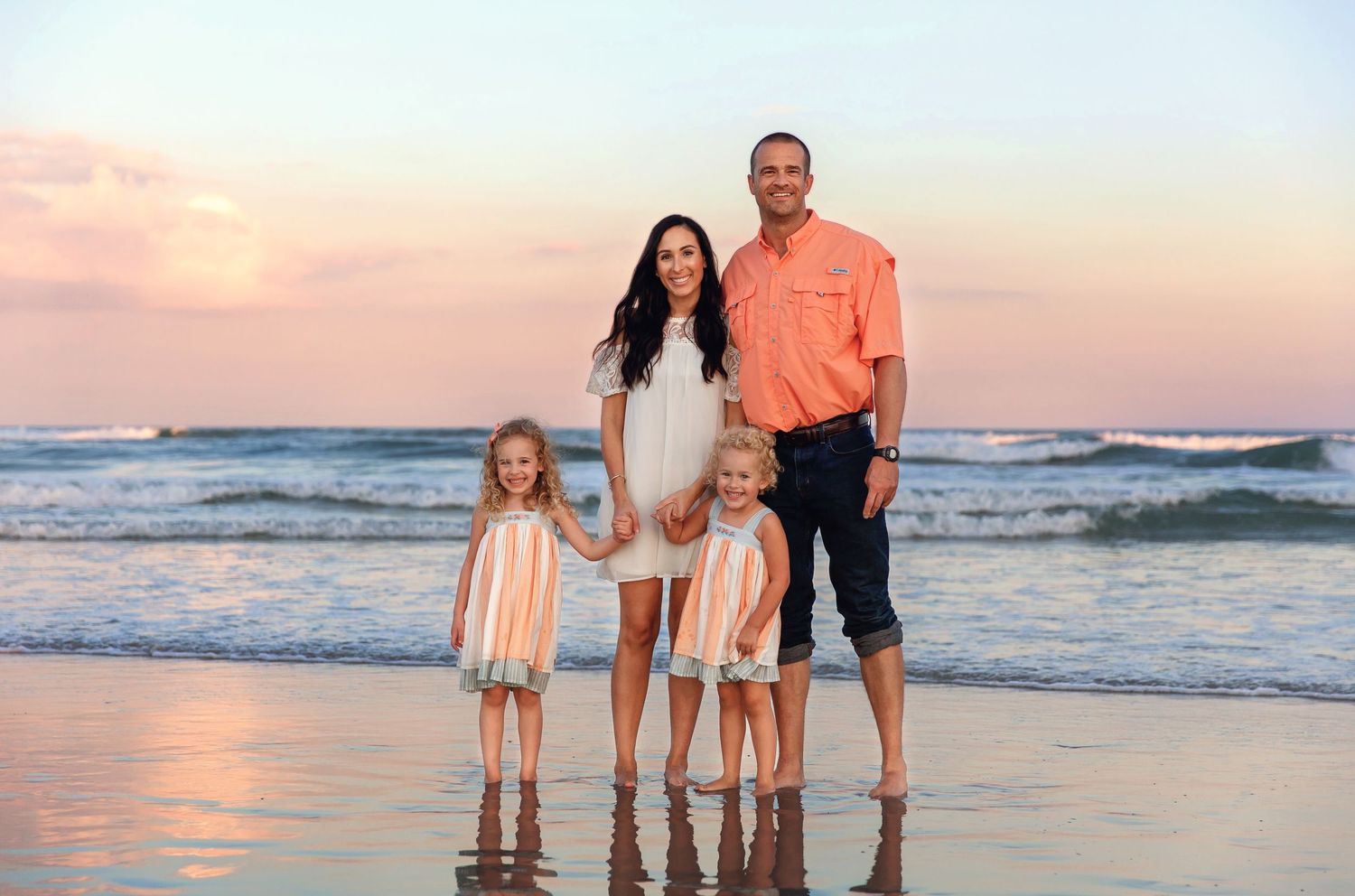 Family standing together on beach at sunset with ocean waves and golden light in background.