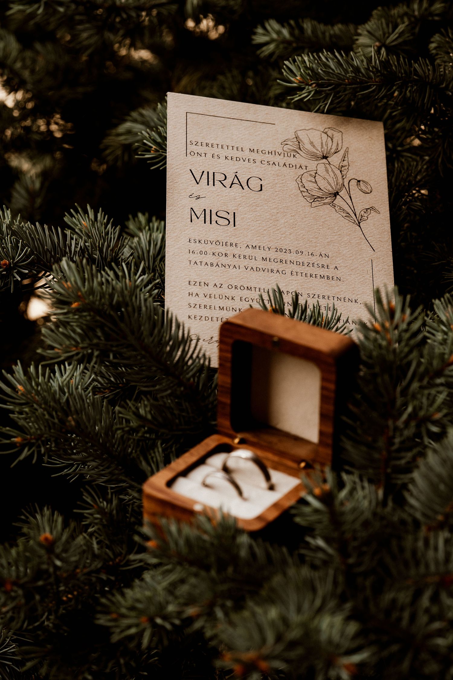 Wedding invitation and ring box nestled in pine branches with soft lighting.