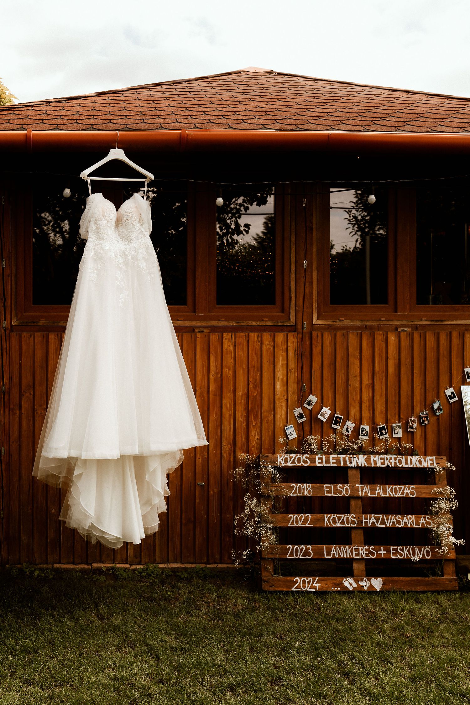 White wedding dress hanging outside a wooden cabin with rustic signage display.