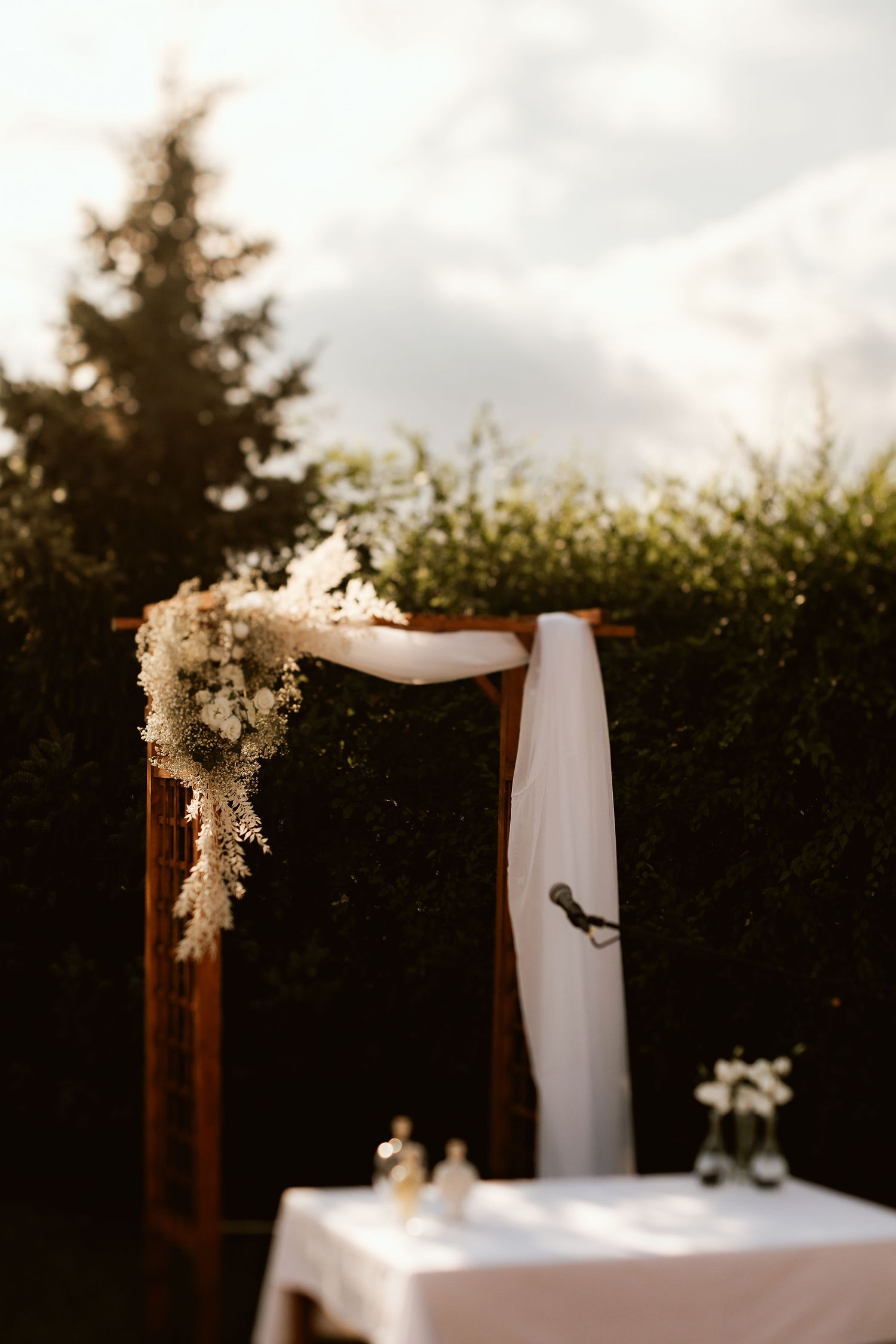 Wooden wedding arch decorated with white fabric and dried flowers at sunset.