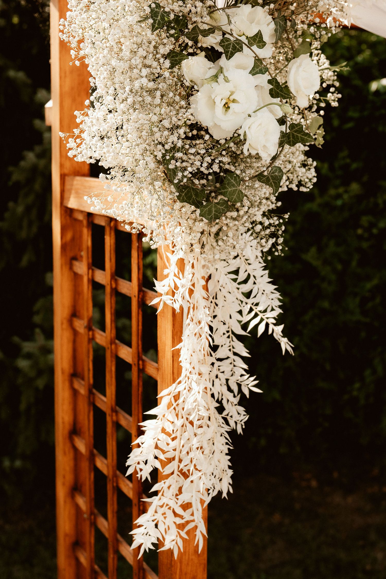 White floral arrangement with baby's breath cascading down wooden lattice.