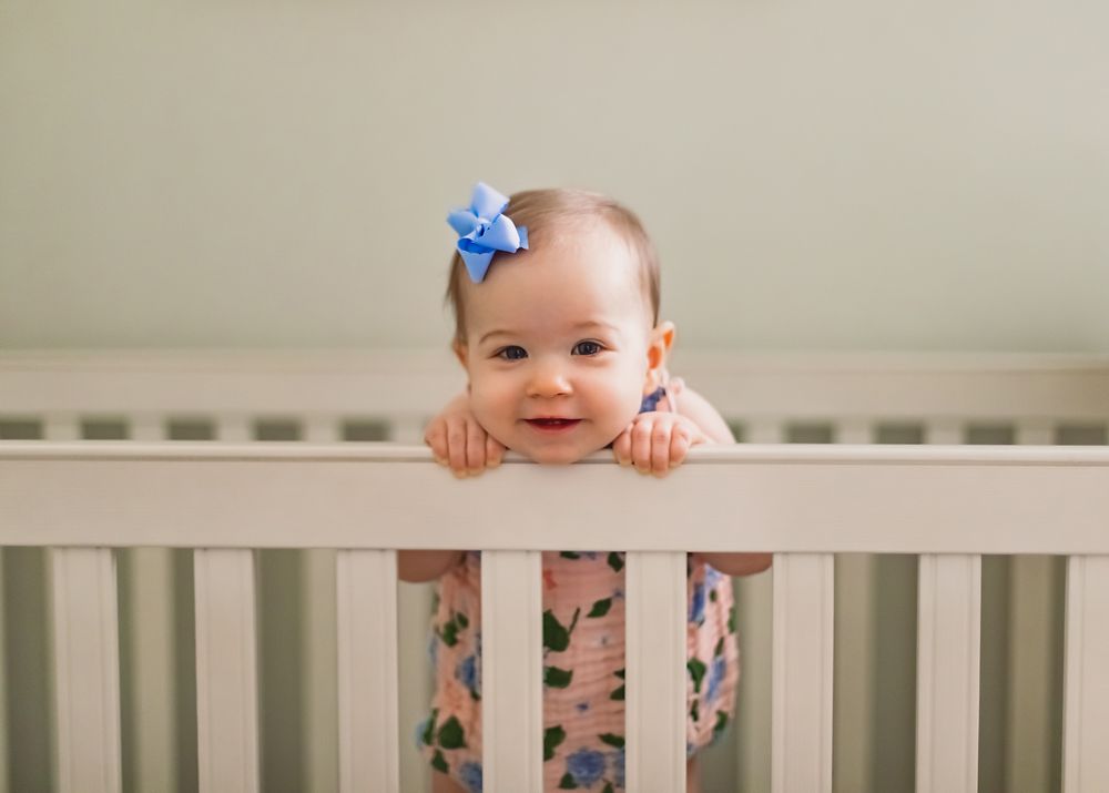 A smiling baby in a white crib wearing a blue bow.