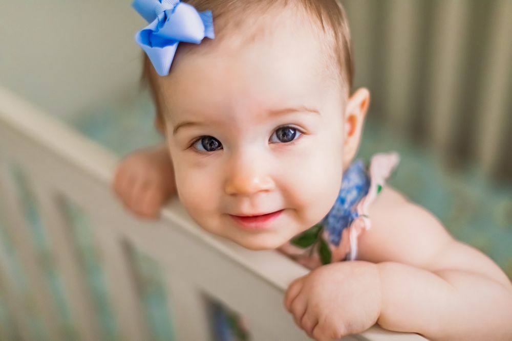 A small child in a crib wearing a blue bow and floral outfit.