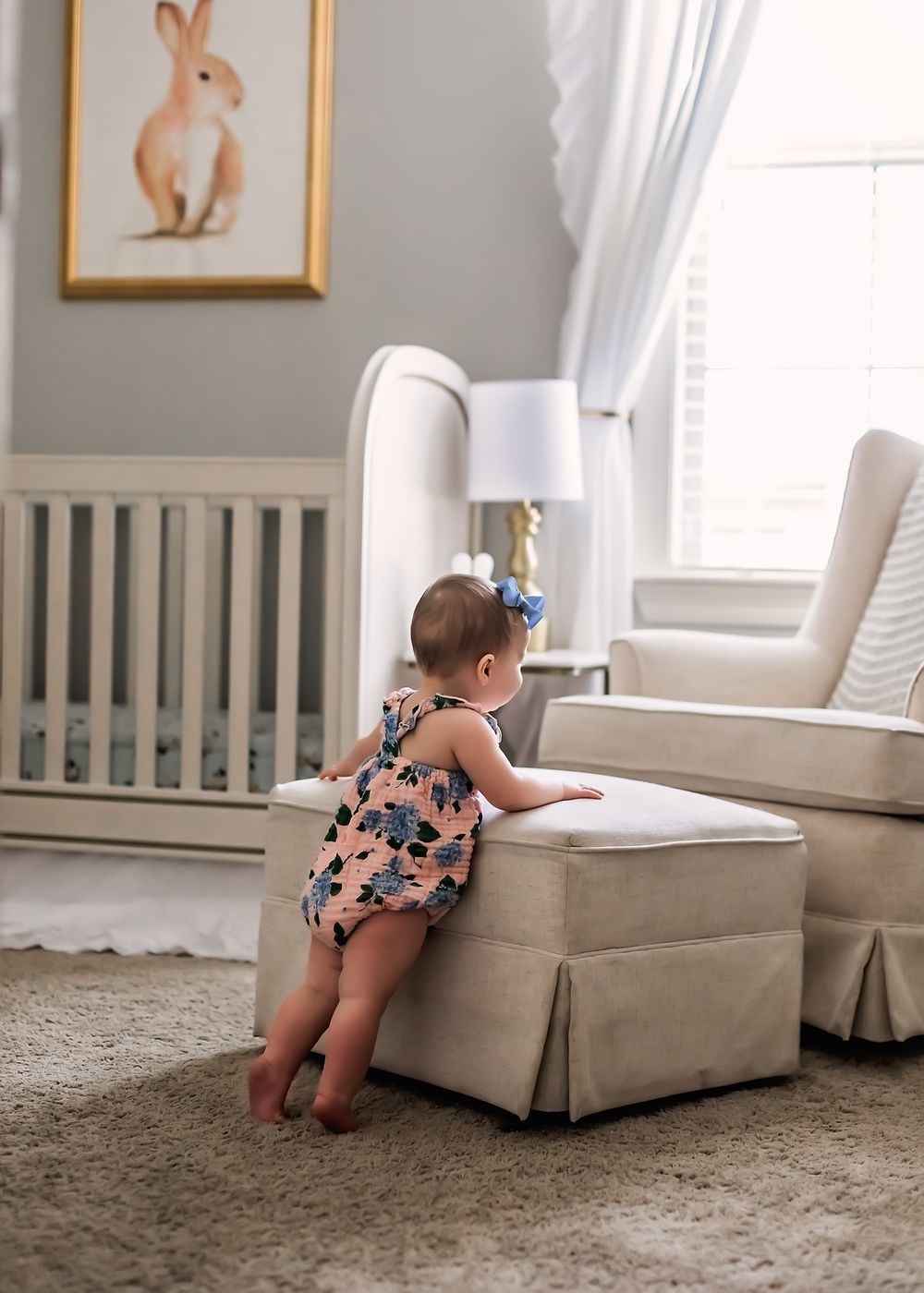 A nursery room with bunny artwork, white furniture, and a child reaching up to a chair.