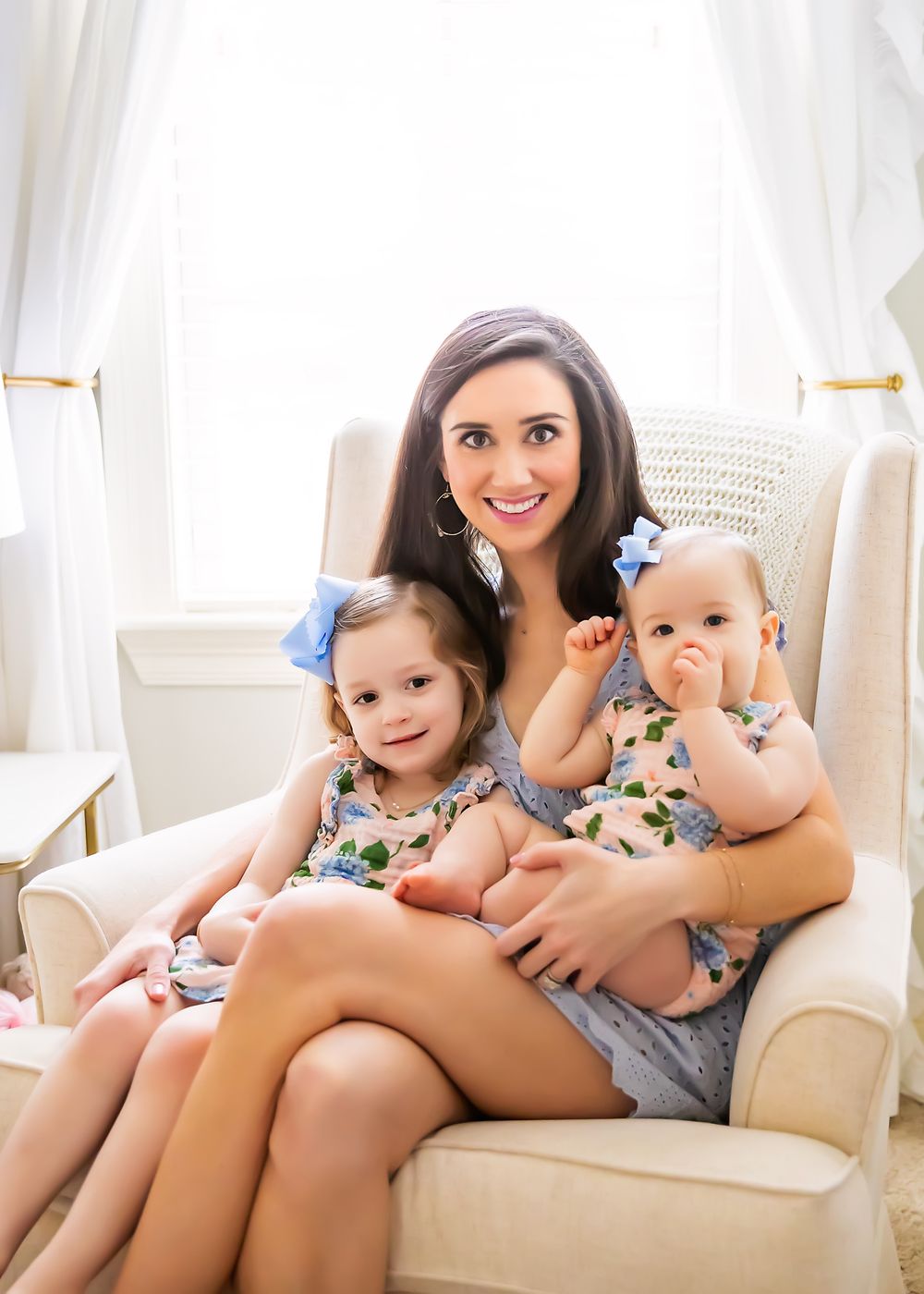 Family portrait of mother with two children sitting in white armchair by window.
