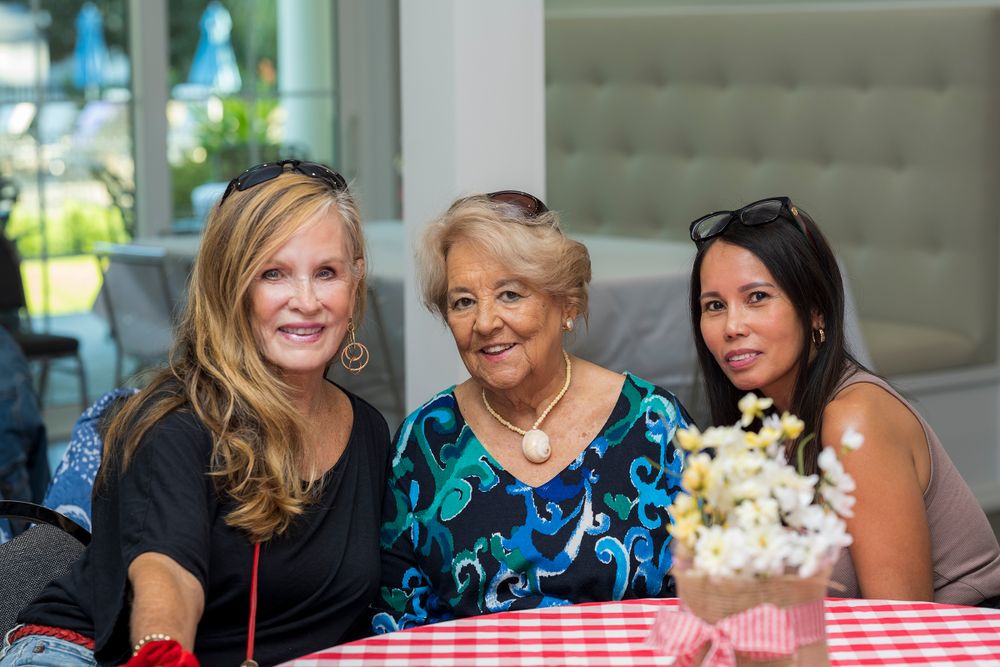 Three women enjoying a casual gathering at a table with red checkered tablecloth and flower centerpiece.