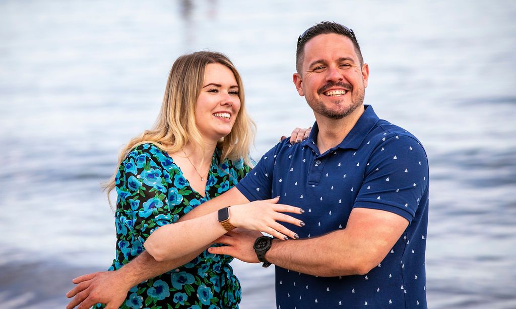 A happy couple laughs together by the ocean wearing coordinated blue patterned outfits.