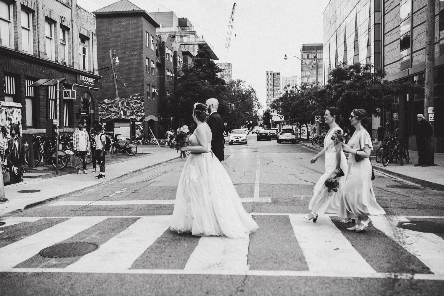 A black and white photo shows wedding party  crossing a busy downtown Toronto street-Alexis Anne Photography-Muskoka Wedding Photographer